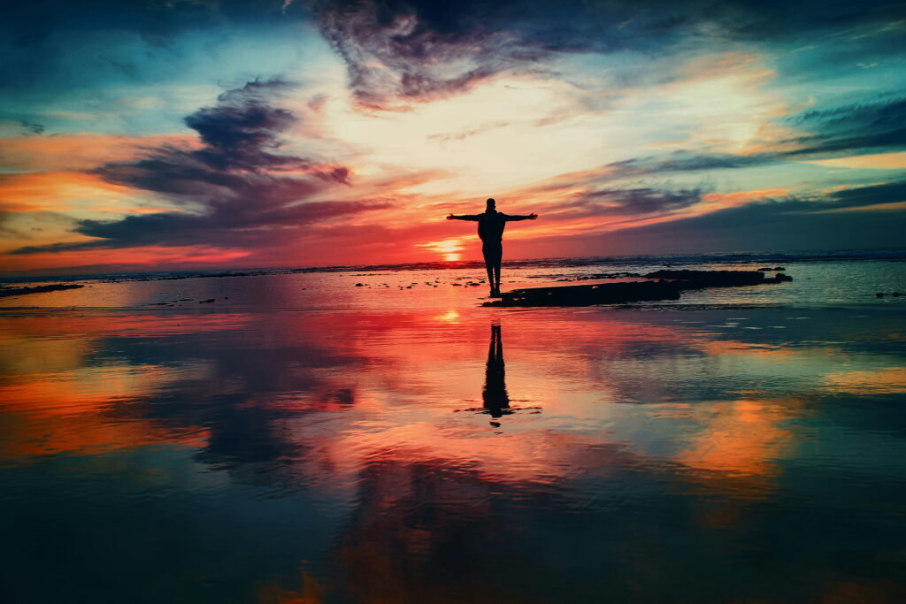 freedom from drinking alcohol - sunset midlife woman with arms out wide on the beach